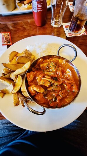 A plate with a bowl of curry and fries, a bottle of ketchup, and a glass of water on a wooden table. - The Queens Head (Durham)