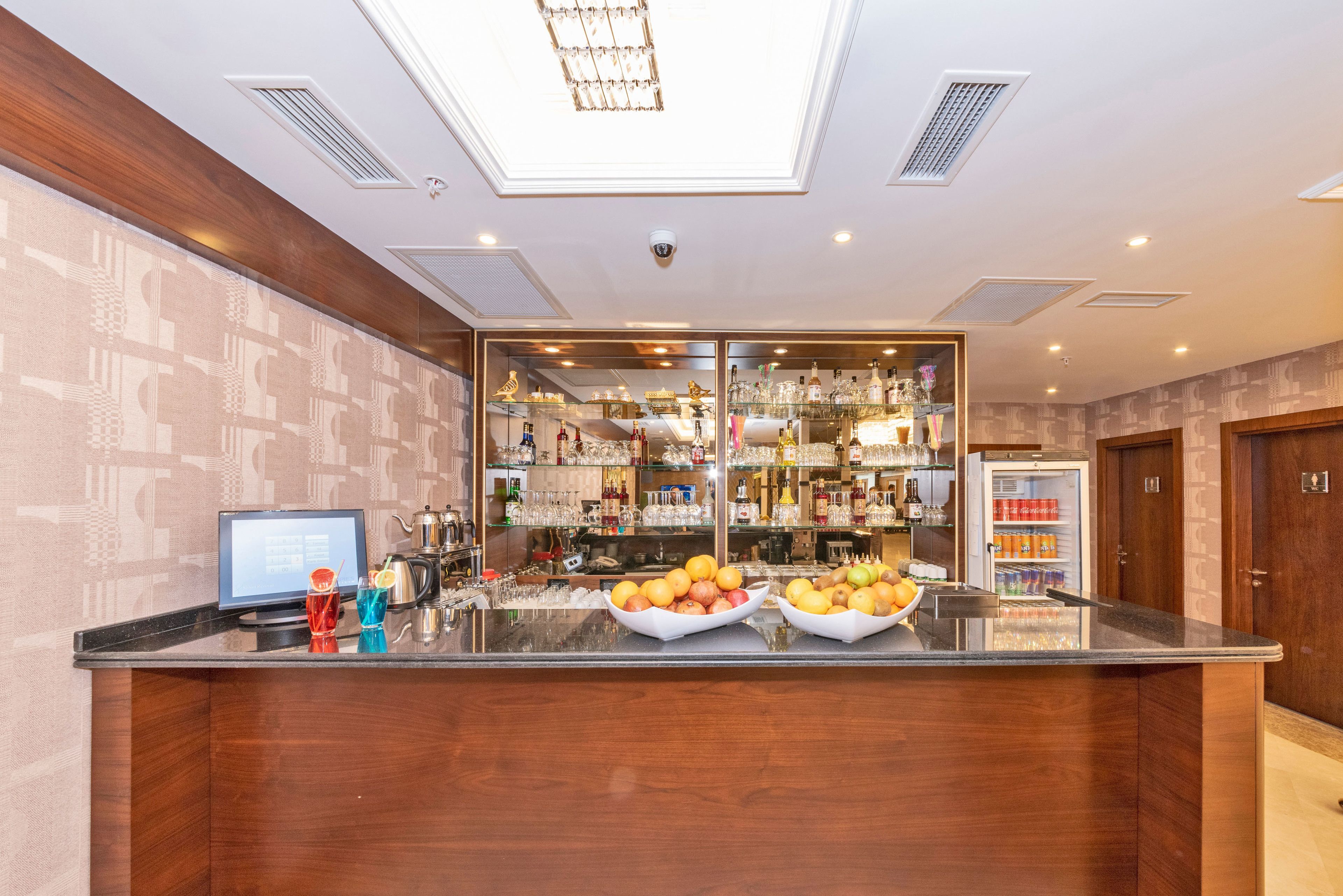A hotel reception area with a modern design, featuring a glass partition, a digital display, and a fruit bowl on the counter.