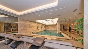 A modern indoor pool area with lounge chairs, a central pool, and a staircase leading to an upper level. - Piya Sport Hotel (Istanbul)