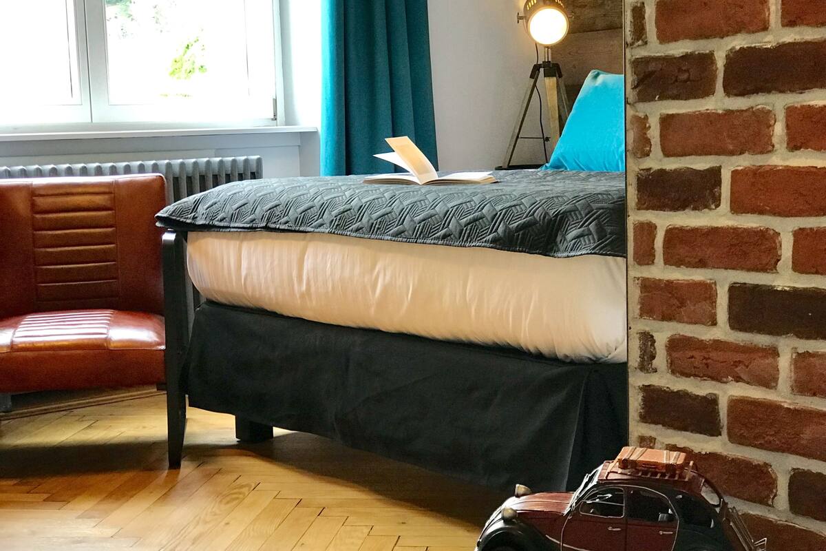 Een slaapkamer met een bed, een stoel, een lamp en een speelgoedautootje.