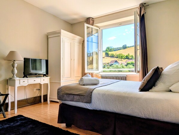 Une chambre à coucher avec un lit, un téléviseur posé sur un bureau, une armoire et une fenêtre donnant sur un paysage.