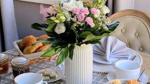 Une table de petit-déjeuner avec un vase de fleurs, du pain, des viennoiseries et des produits laitiers.