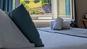 Une chambre avec une grande fenêtre, un lit avec des oreillers et une vue sur un paysage verdoyant.