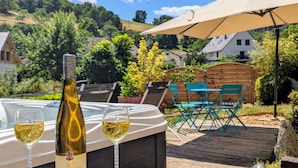 Un bain à remous, deux verres de vin, une terrasse en bois, du mobilier d’extérieur et une vue sur une colline.