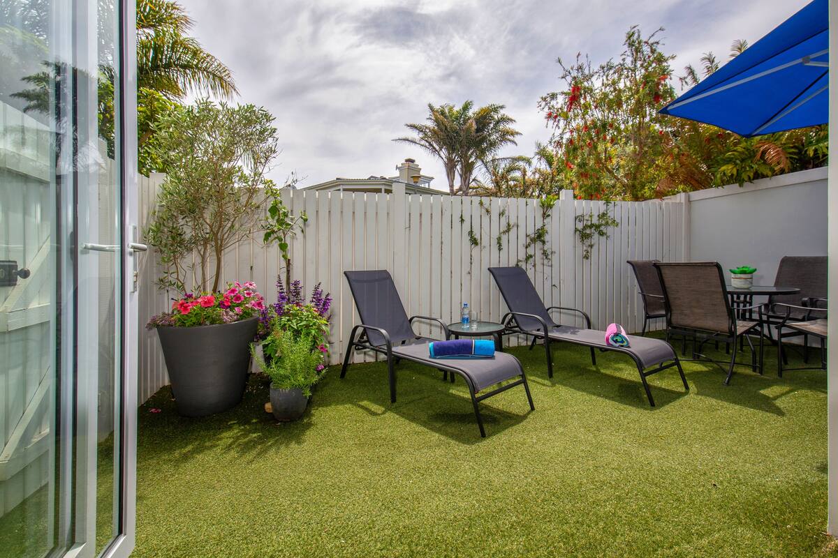A backyard with artificial grass, a white fence, and outdoor furniture including two lounge chairs and a table.