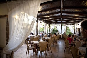 Ein Restaurant im Freien mit Korbmöbeln und weißen Vorhängen.