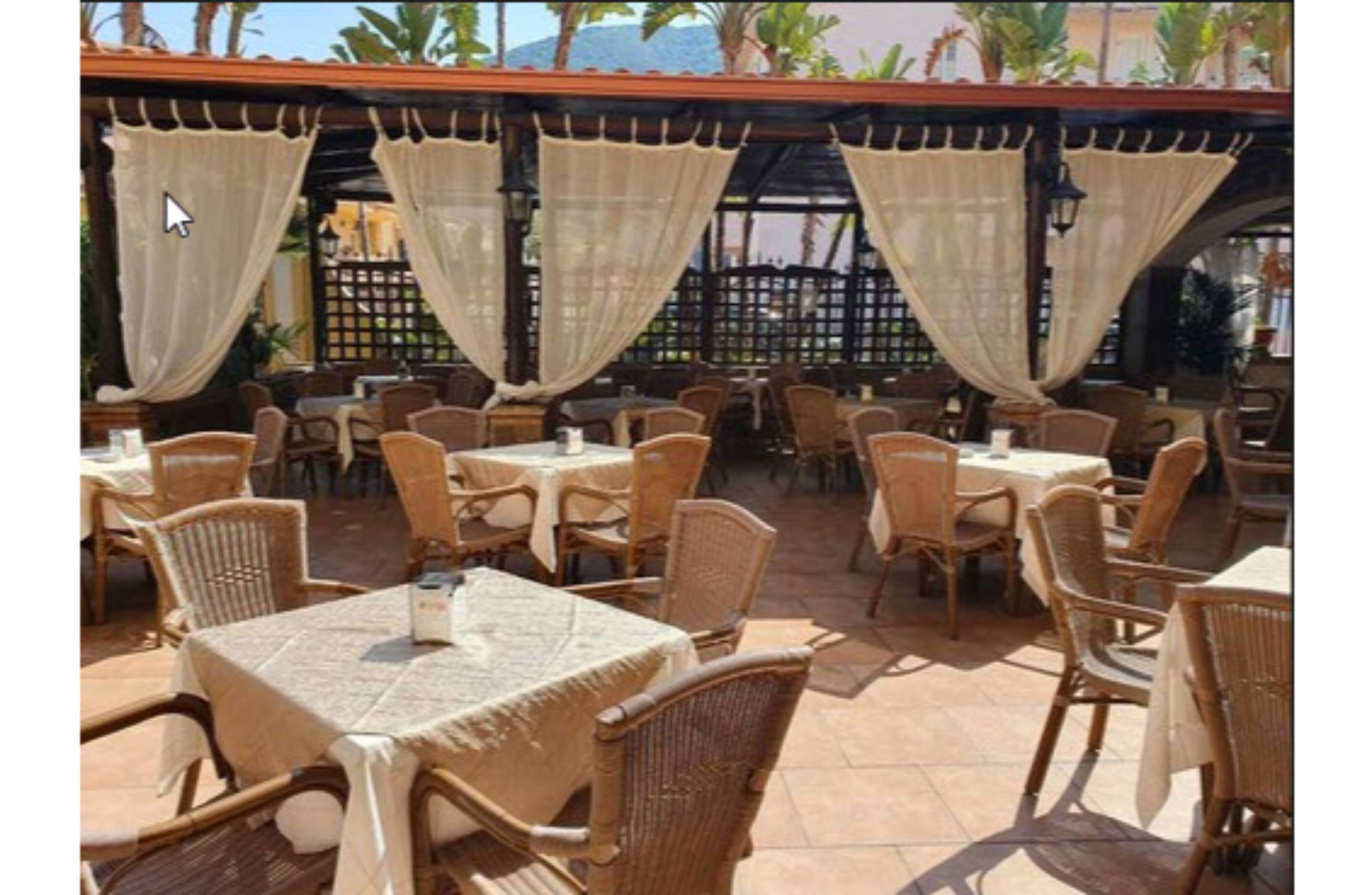 An outdoor patio area with wicker tables and chairs, covered by beige curtains.