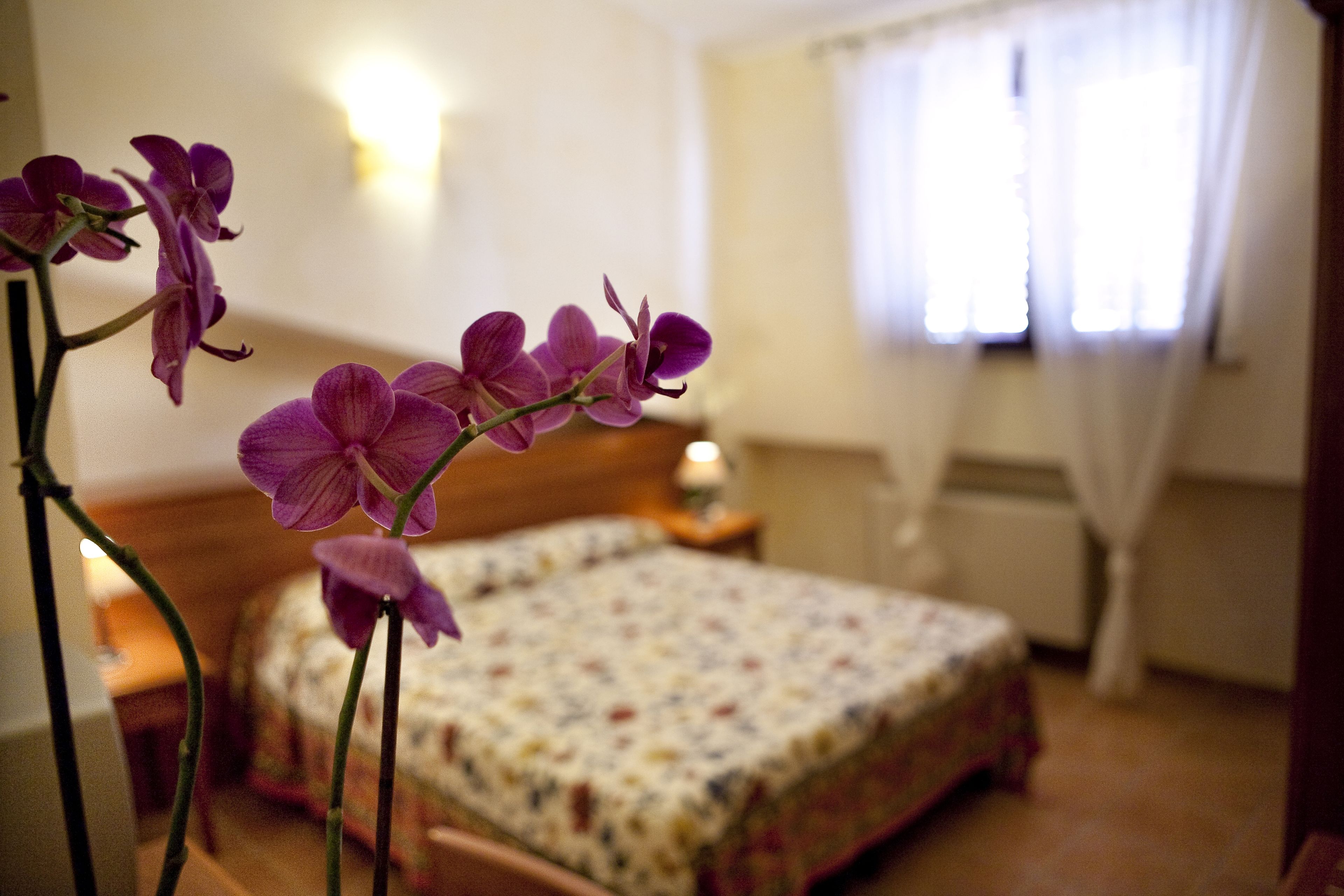 Quarto com cama, mesa de cabeceira e janela com cortinas.