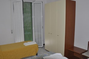 Um quarto com cama, guarda-roupa e uma pequena mesa.