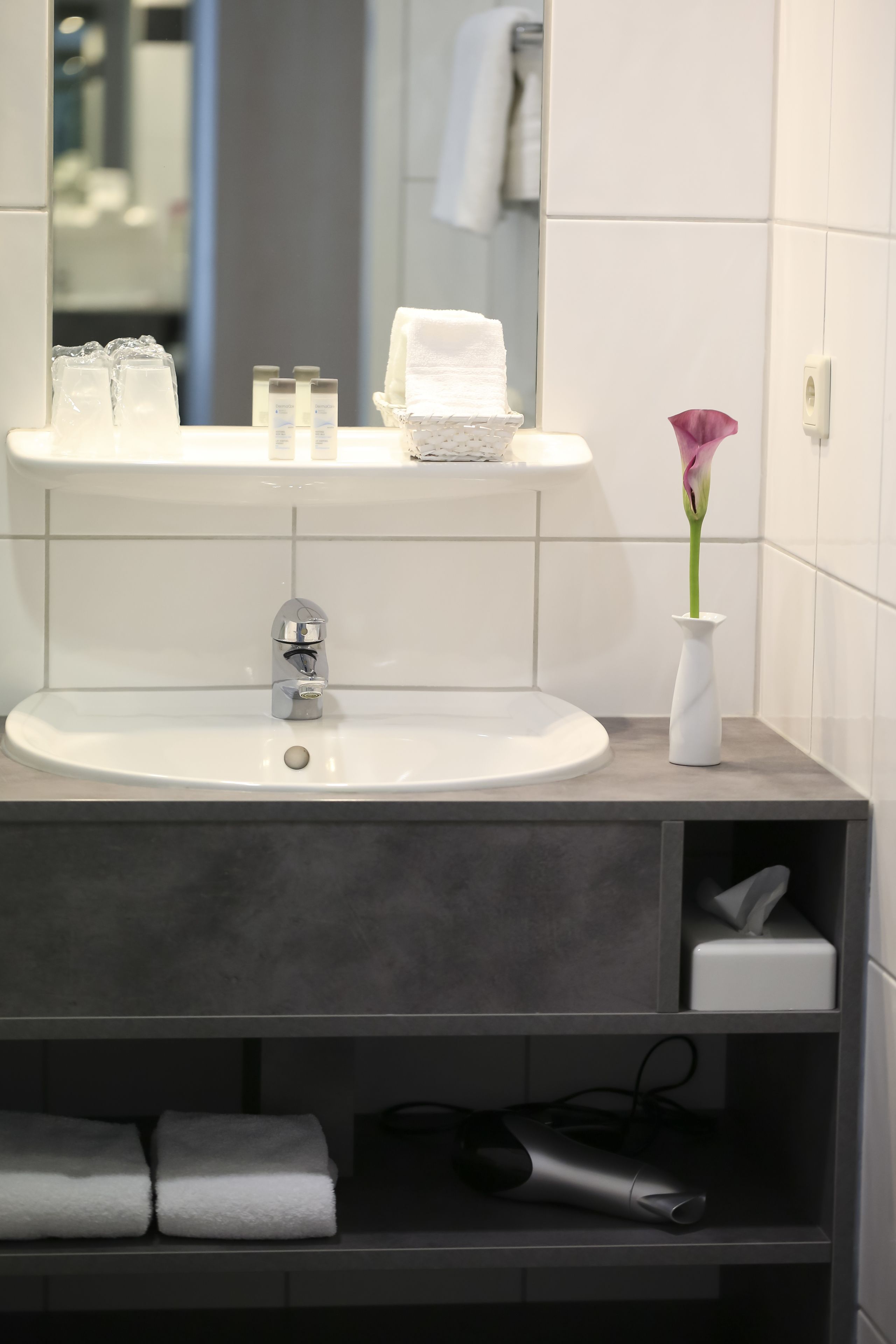 A bathroom with a white sink, a mirror, a vase with a flower, and a towel rack.
