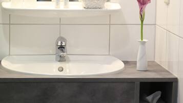 A bathroom with a white sink, a mirror, a vase with a flower, and a towel rack.