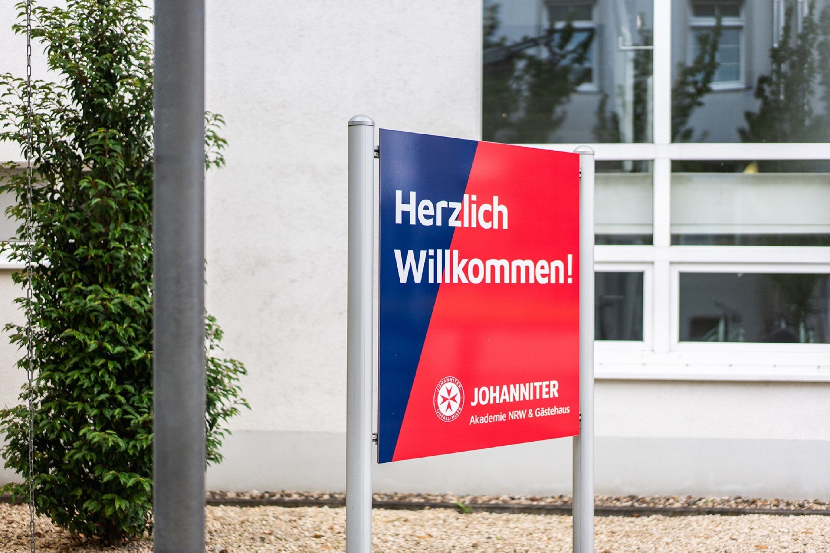 Ein Willkommensschild mit der Aufschrift "Herzlich Willkommen!" und "JOHANNITER", befestigt an einem Metallpfosten.