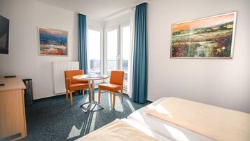 Une chambre d’hôtel avec un lit, un bureau, une chaise, une table et deux tableaux accrochés aux murs.