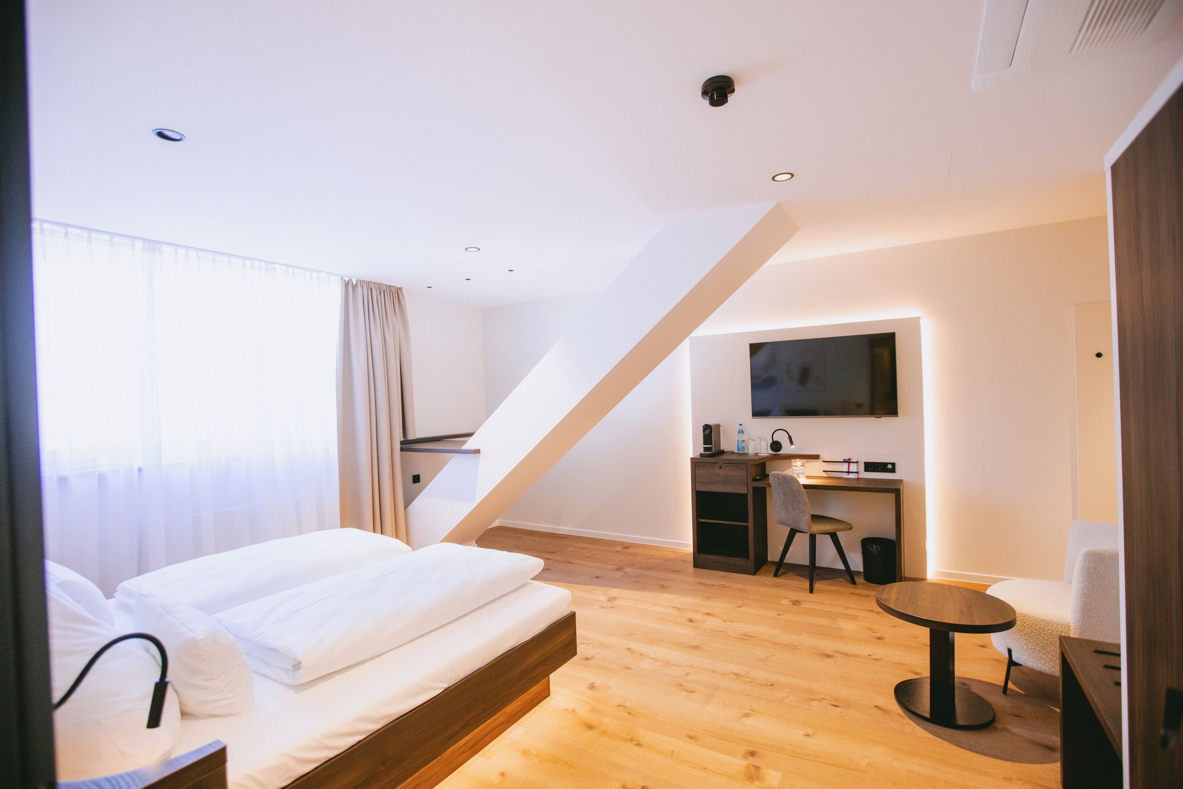 A modern hotel room with a bed, a desk, and a chair.