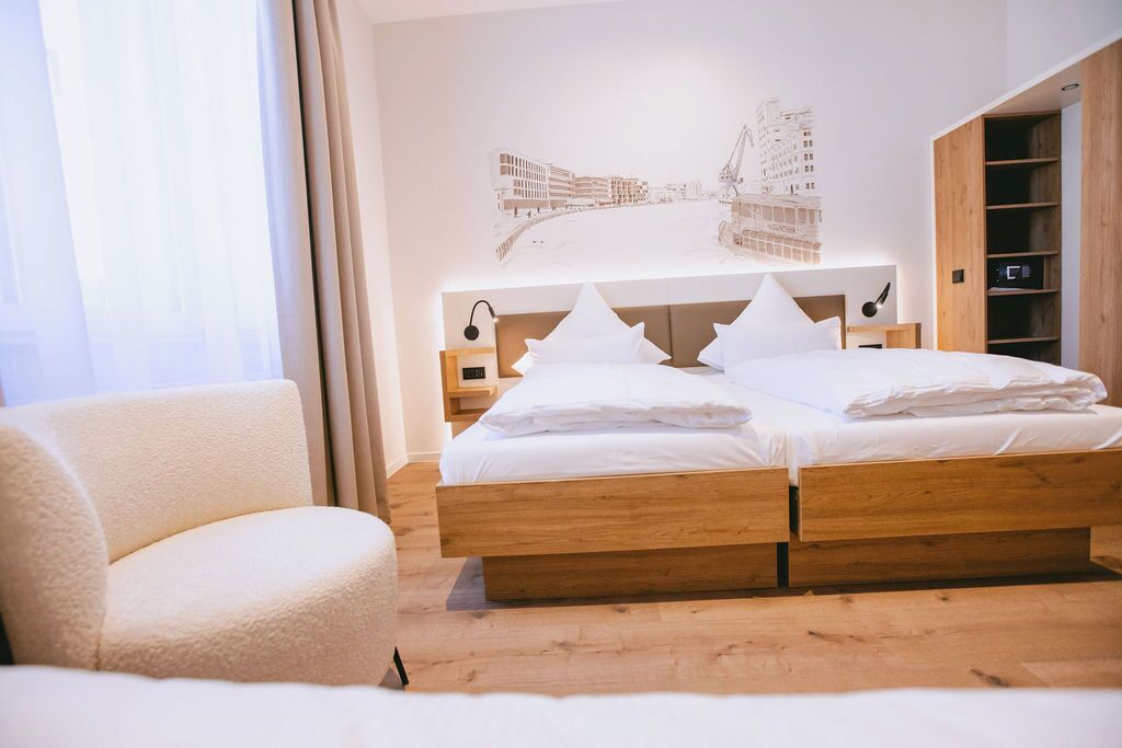 Une chambre avec un lit en bois, une chaise, une étagère fixée au mur et une œuvre d’art représentant un paysage urbain.