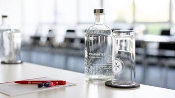 A clear glass bottle and a glass with a logo on a table in a bright room with large windows.