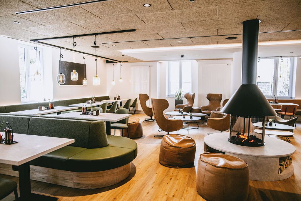 A modern dining area with booths, round tables, and a central fireplace.