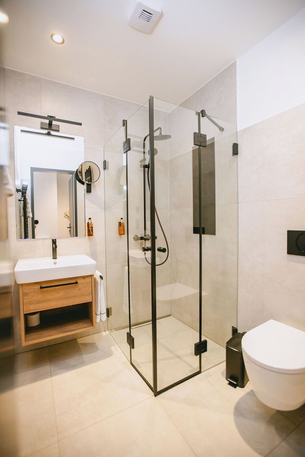 Ein modernes Badezimmer mit einer Duschkabine aus Glas, einem Holzwaschtisch und einer weißen Toilette.