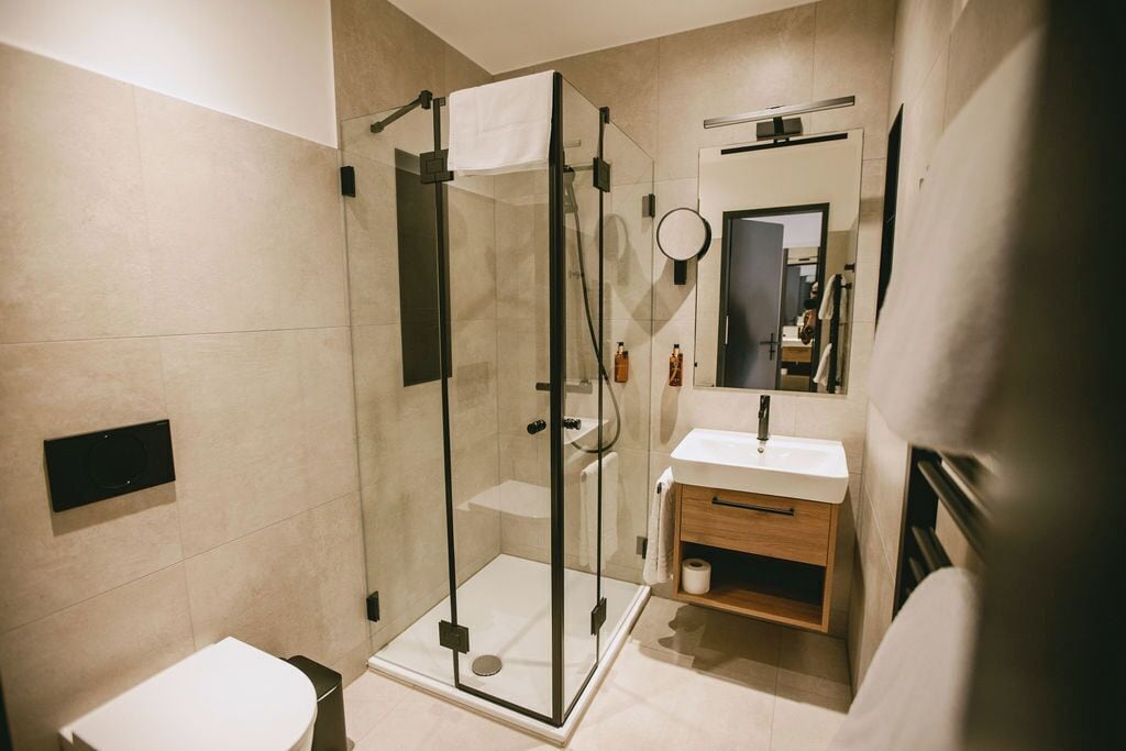 Un baño moderno con ducha envuelta en vidrio, un lavamanos blanco y un espejo.