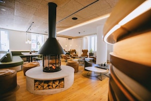 Un interior moderno con chimenea central, zonas de estar y luz natural proveniente de ventanas.