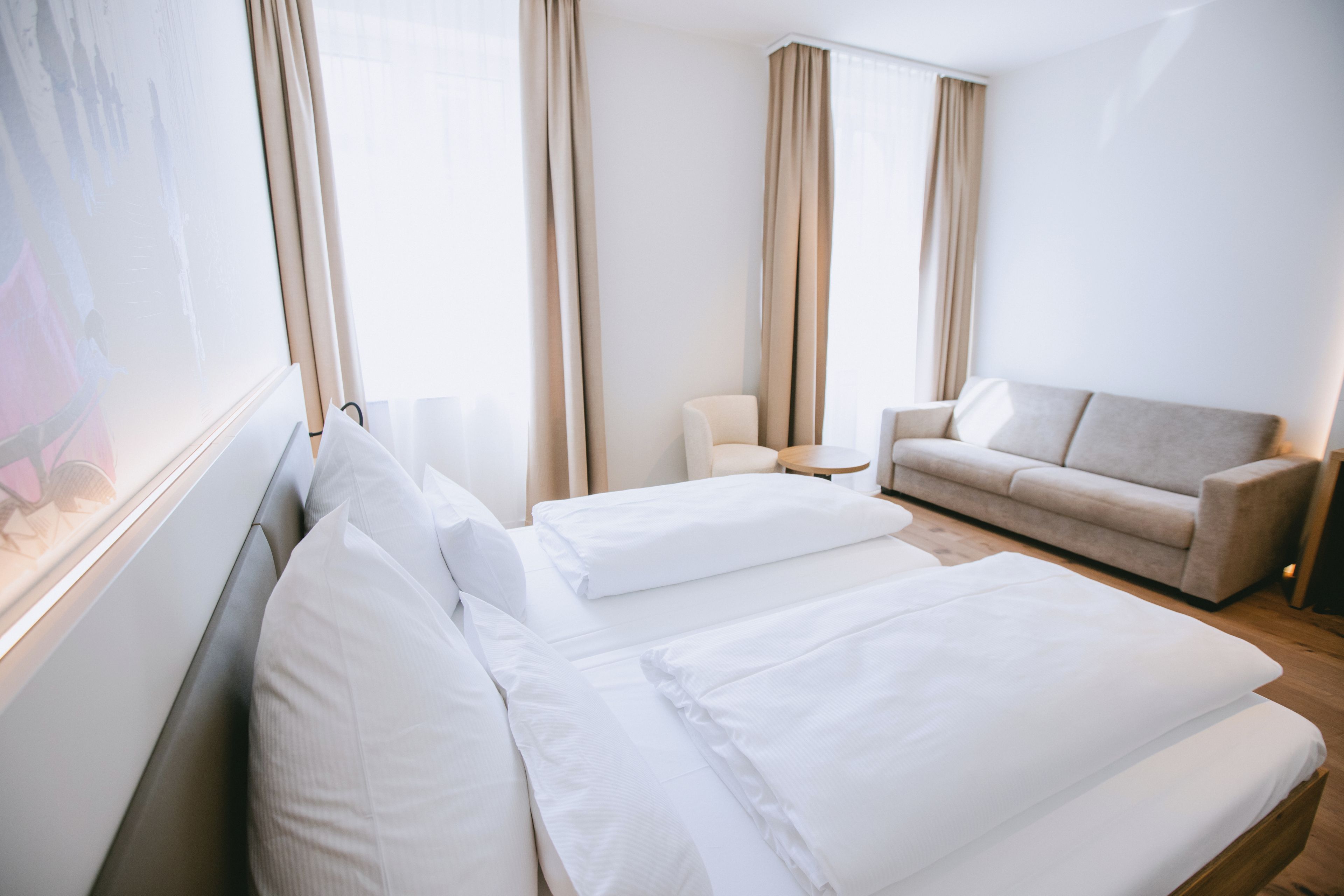 Une chambre d’hôtel avec un lit, un canapé, une chaise et une grande fenêtre.