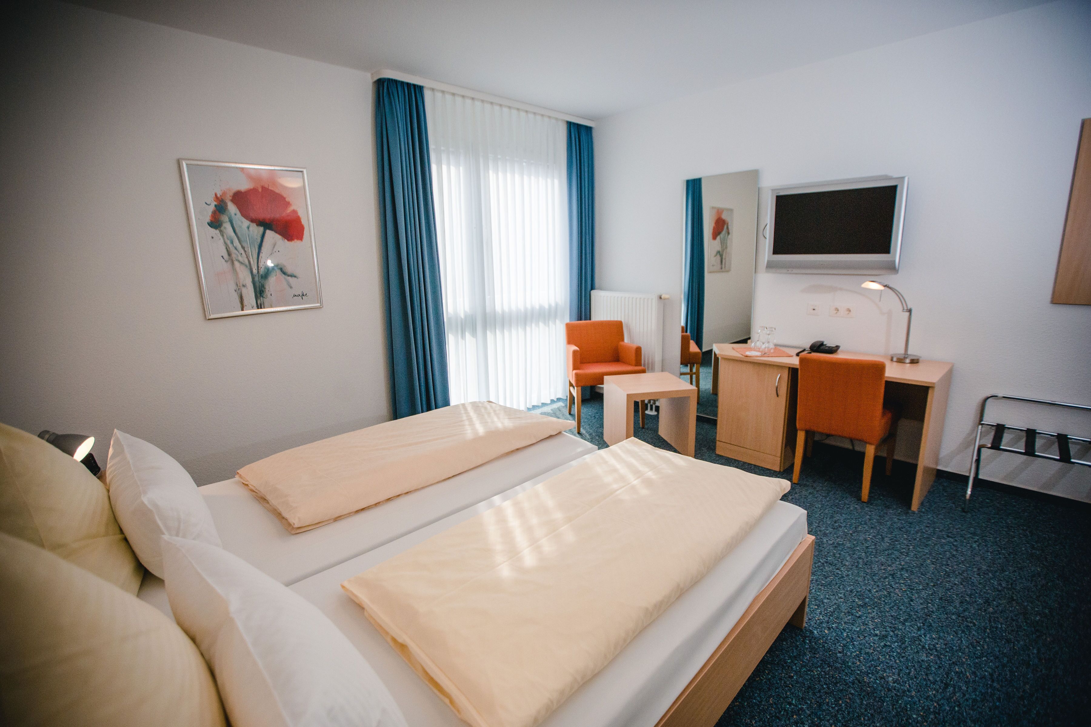 A hotel room with two beds, a desk, a chair, a TV, and a painting on the wall.
