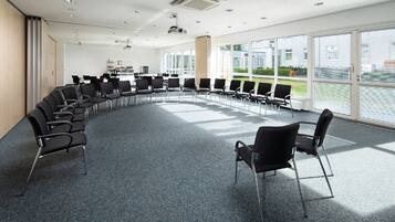 A conference room with a semi-circular arrangement of chairs, large windows, and a projector on the ceiling.