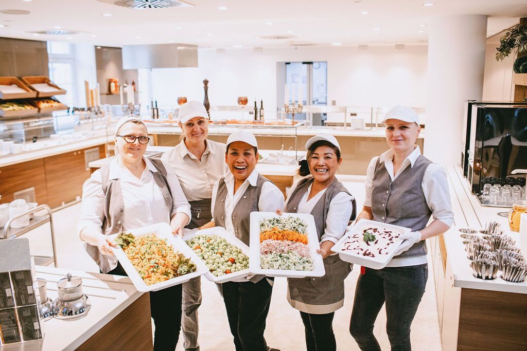 A group of five people in a modern kitchen holding trays of food.