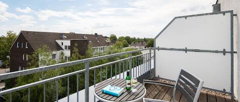 A balcony with a table, a chair, a book, a bottle, and a glass.