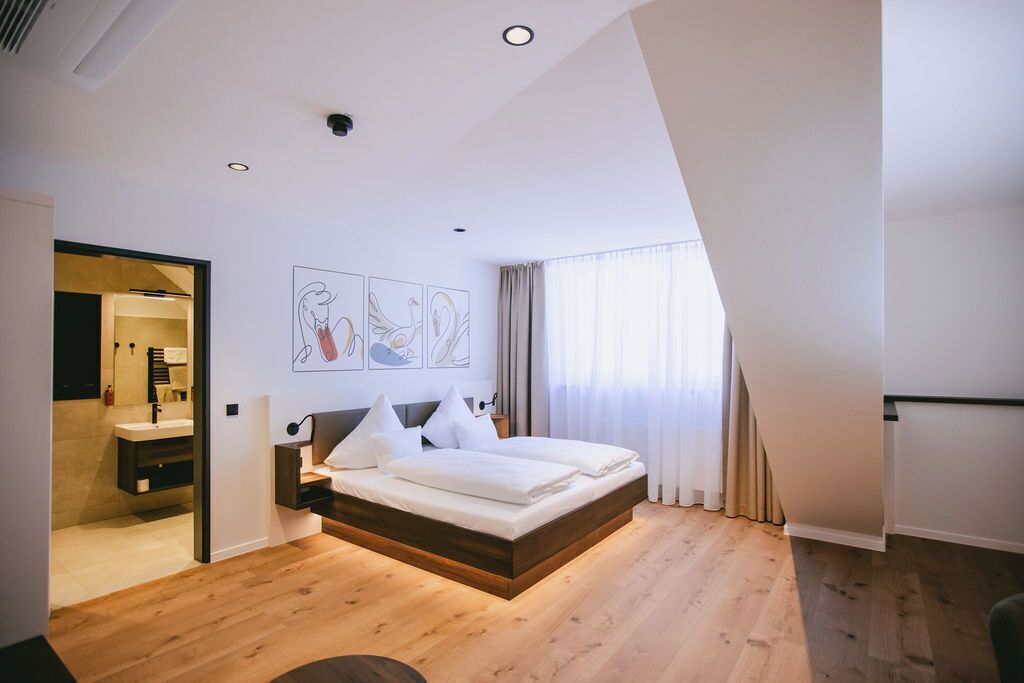 Ein modernes Schlafzimmer mit Holzboden, einem Bett mit weißer Bettwäsche, einem Nachttisch und einem Wandbild.