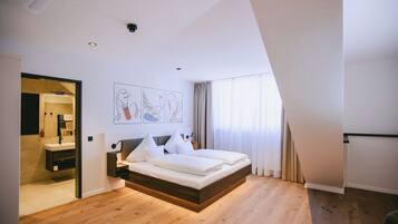 Ein modernes Schlafzimmer mit Holzboden, einem Bett mit weißer Bettwäsche, einem Nachttisch und einem Wandbild.