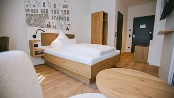 A modern hotel room with a wooden bed, a bedside table, a lamp, and a wall-mounted artwork.