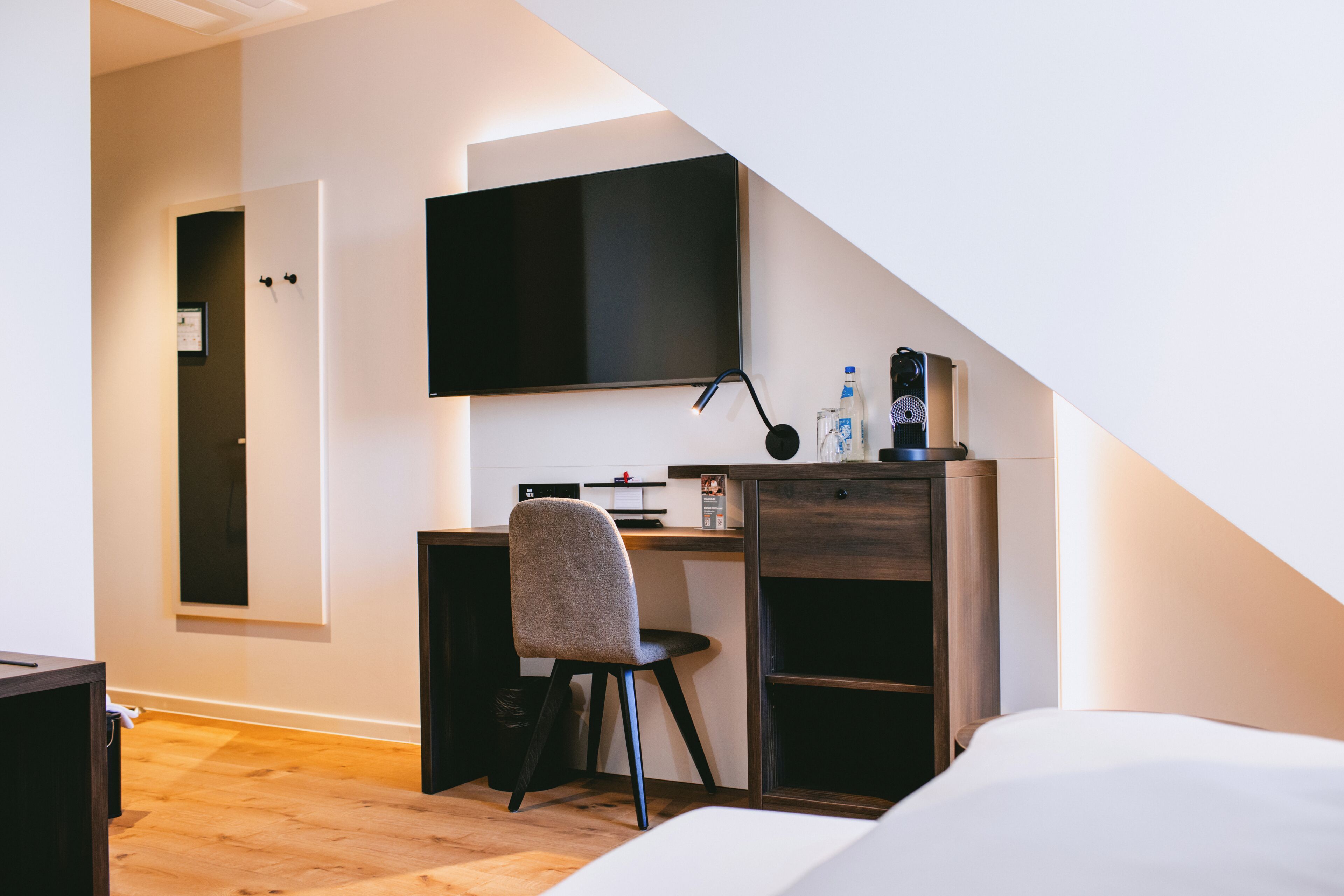 A modern bedroom with a desk, chair, and a flat-screen TV mounted on the wall.