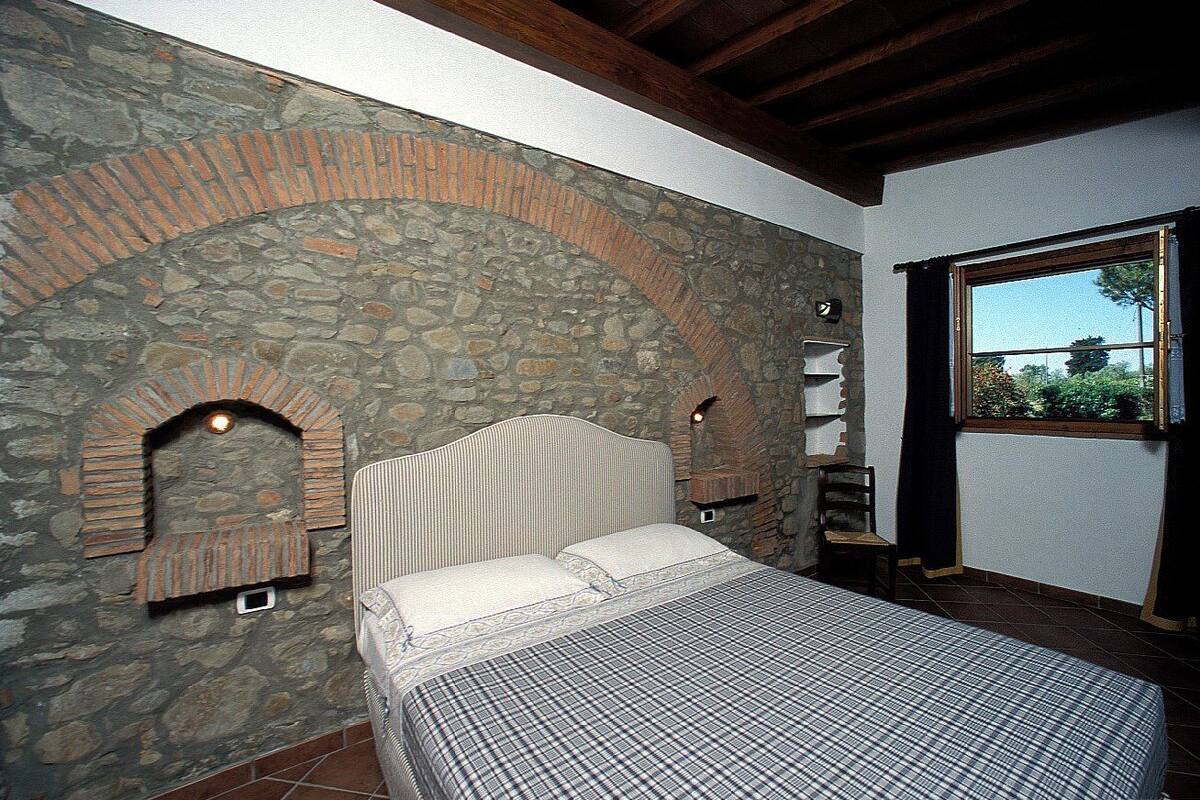 Une chambre avec un mur en pierre, un lit, une fenêtre et une cheminée.