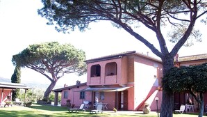 Ein zweistöckiges Haus mit Terrasse, Sitzgelegenheiten im Freien und einem großen Baum.