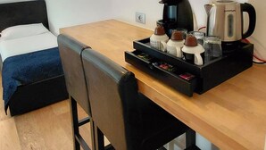 Een hotelkamer met een bed, een houten tafel met een dienblad met ontbijtartikelen, een koffiezetapparaat en een waterkoker.