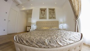 Een slaapkamer met een groot bed, een plafond met zichtbare balken en twee wandlampen.