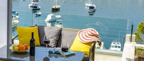 A balcony with wicker furniture, a glass table, and a view of a marina with boats.