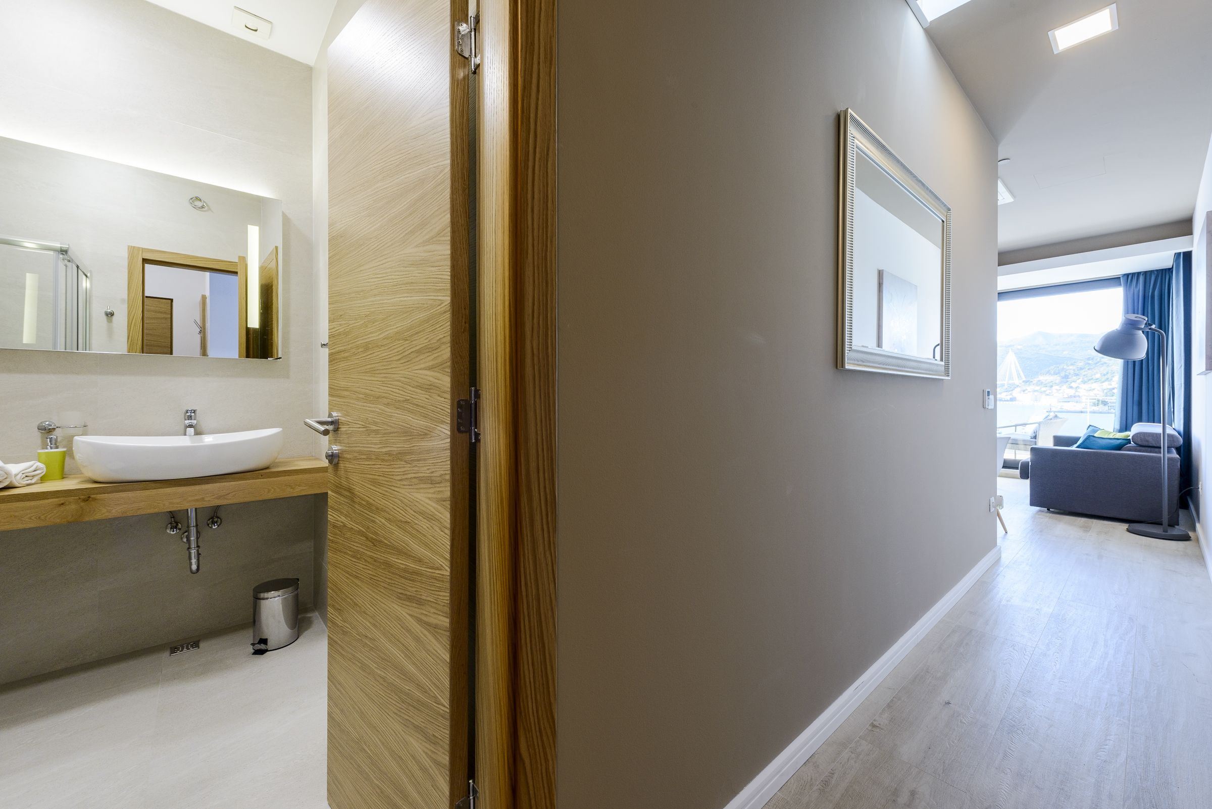 Un baño moderno con puerta de madera, lavamanos blanco y un espejo grande.
