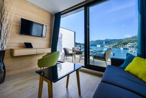 Sala de estar moderna com uma televisão grande, área de jantar e varanda com vista para um porto e montanhas.