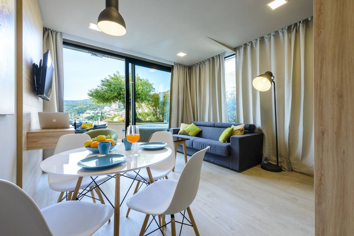 Un salon moderne avec un coin repas, de grandes fenêtres et une vue sur une colline.