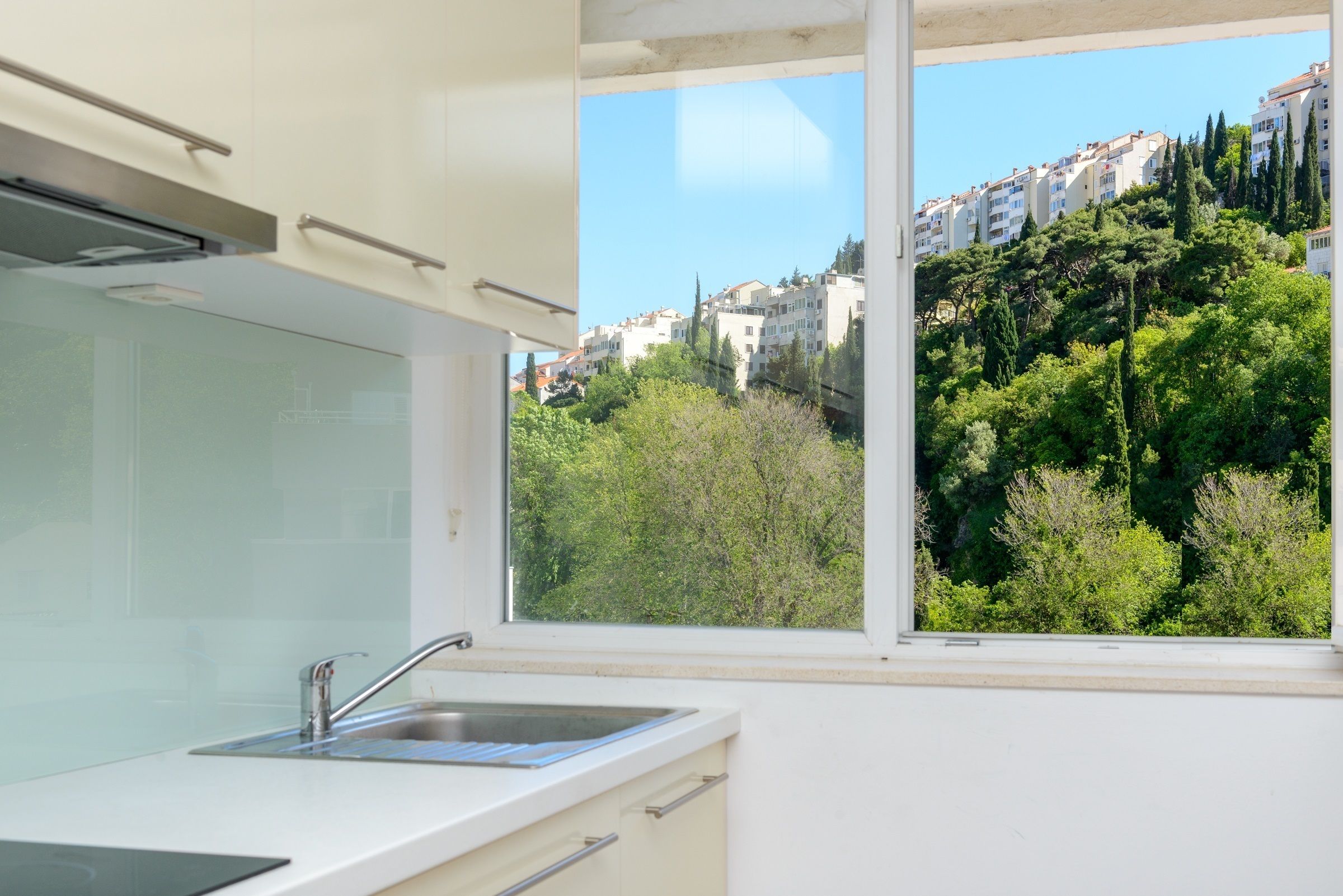 A modern kitchen with a window view of a hillside residential area.