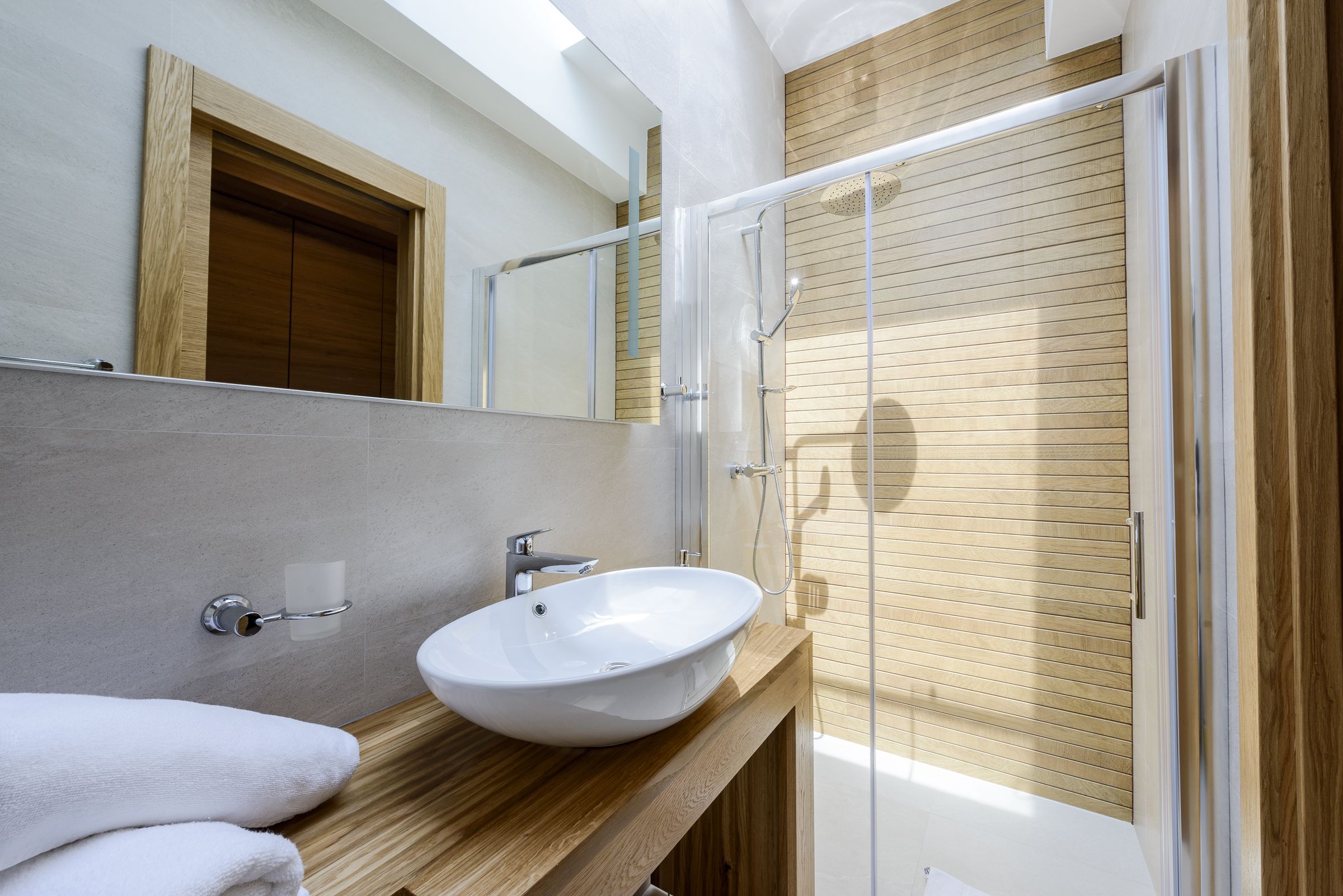 A modern bathroom with a wooden vanity, a white sink, and a glass shower enclosure.
