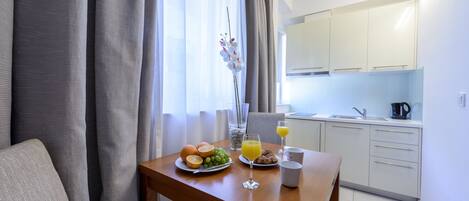 Una mesa de comedor con alimentos para el desayuno, un florero con flores y vista a una cocina y comedor modernos.