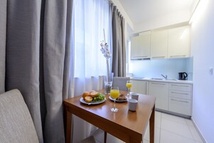 Una mesa de comedor con alimentos para el desayuno, un florero con flores y vista a una cocina y comedor modernos.