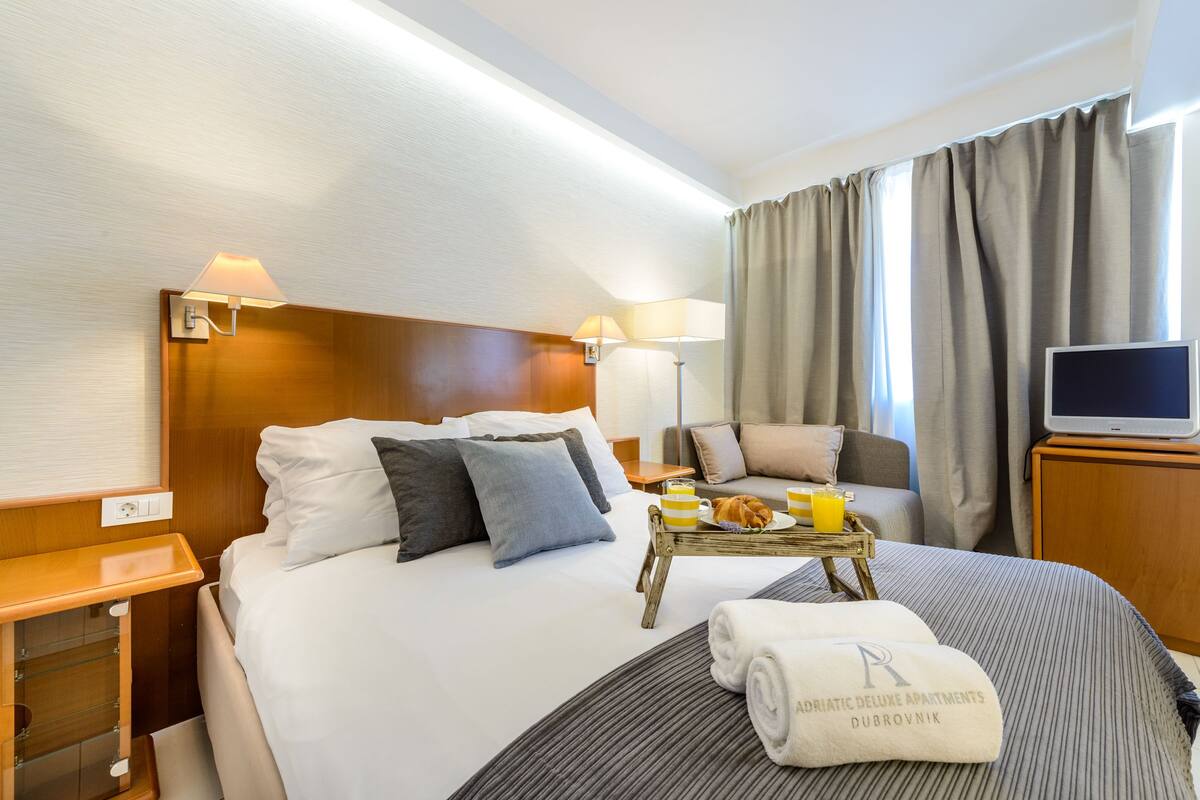 Une chambre d’hôtel équipée d’un lit, d’une table de chevet, d’une lampe, d’une télévision et d’un plateau de petit-déjeuner.