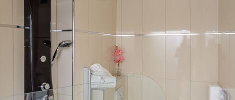 A modern bathroom with a glass-enclosed shower, a towel rack with a white towel, and a small vase with pink flowers on the wall.