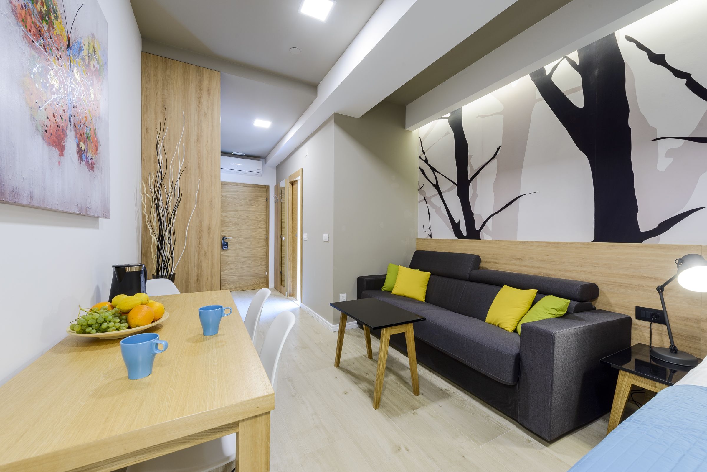 Una sala moderna con sofá, mesa de centro y mesa de comedor con fruta y tazas.