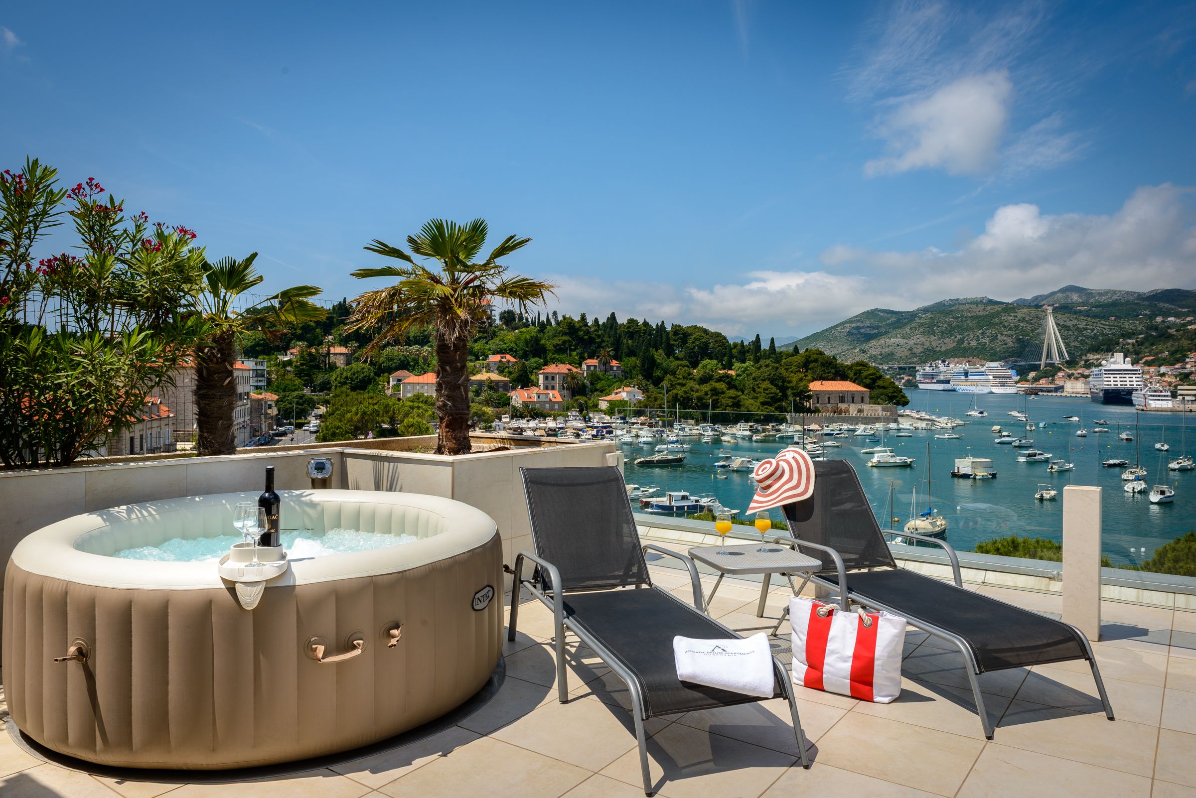 A rooftop terrace with a hot tub, lounge chairs, and a view of a marina with boats and a bridge.