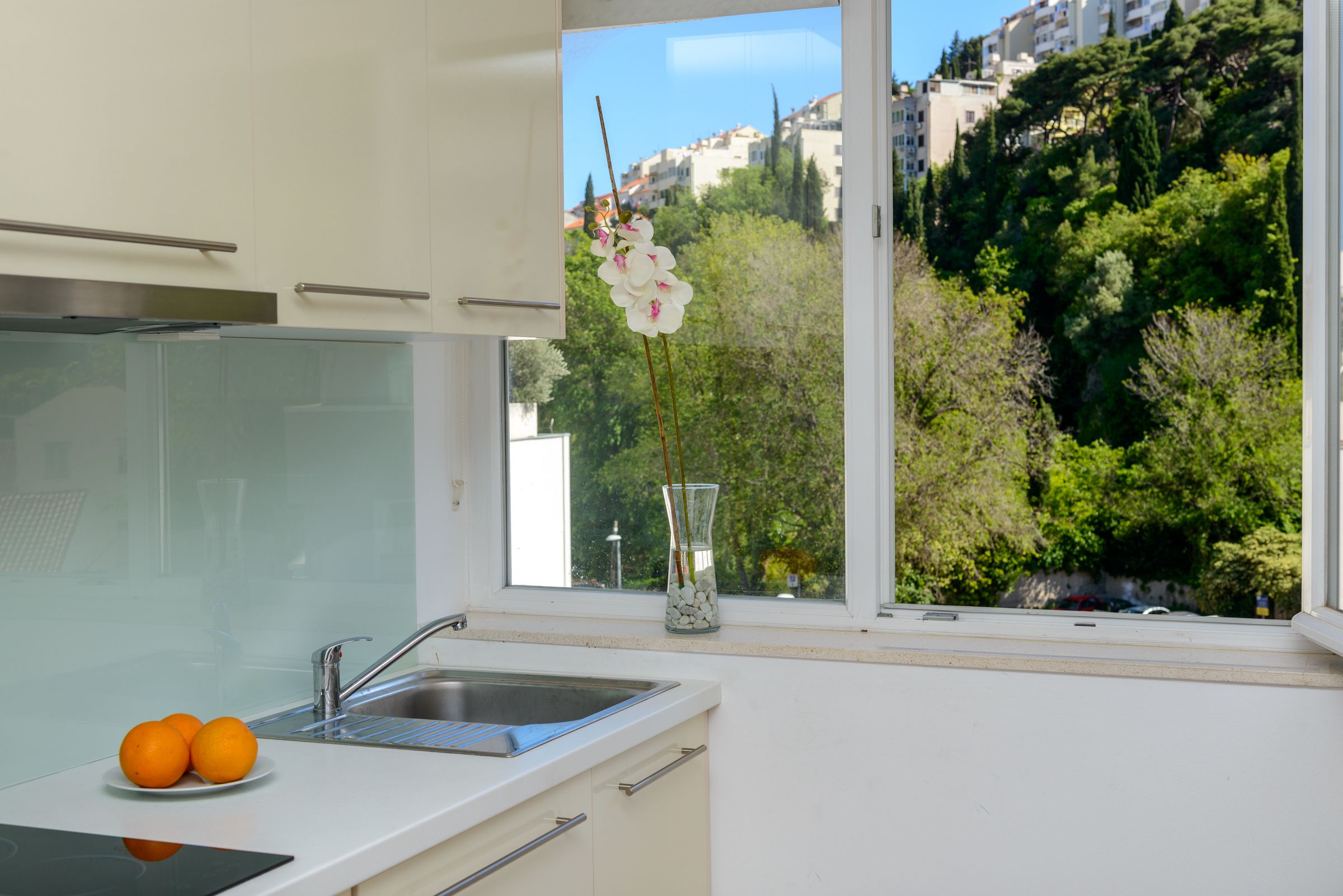 Una cocina moderna con un lavamanos, un plato de naranjas y un jarrón con flores en el alféizar de la ventana.